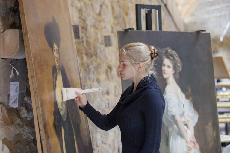 A painting conservator brushing superficial dust from the surface of a painting at The Royal Oak Conservation Studio, Knole Barn, Kent. Photography: Megan Taylor National Trust Images.